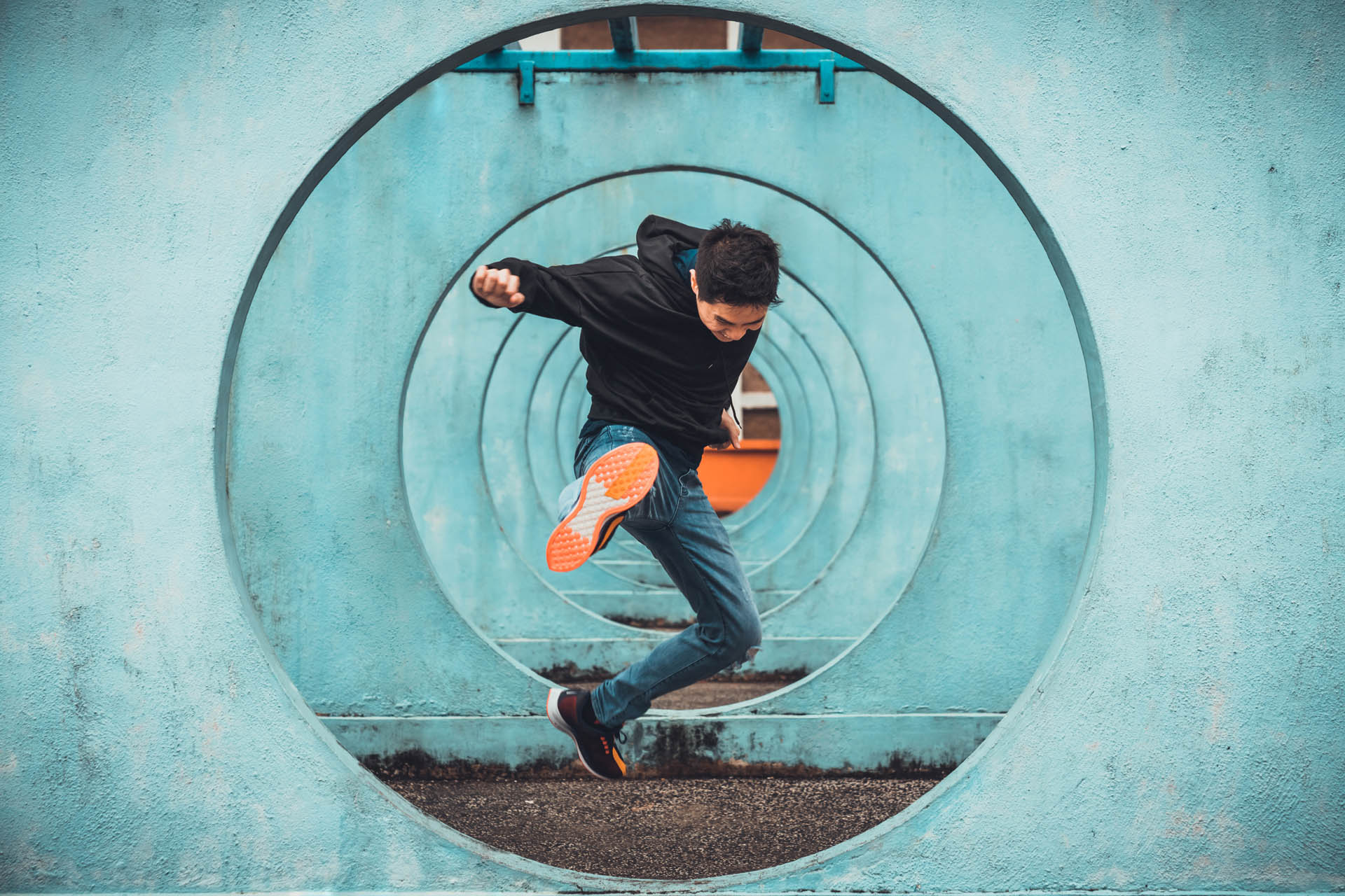 Young Asian active man in action of jumping and kicking, circle looping wall background. Extreme sport activity, parkour outdoor free running, or healthy lifestyle concept
